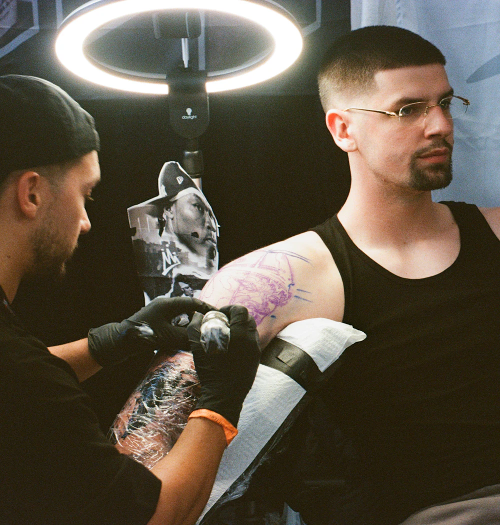 A tattoo artist working on a client's arm under a ring light